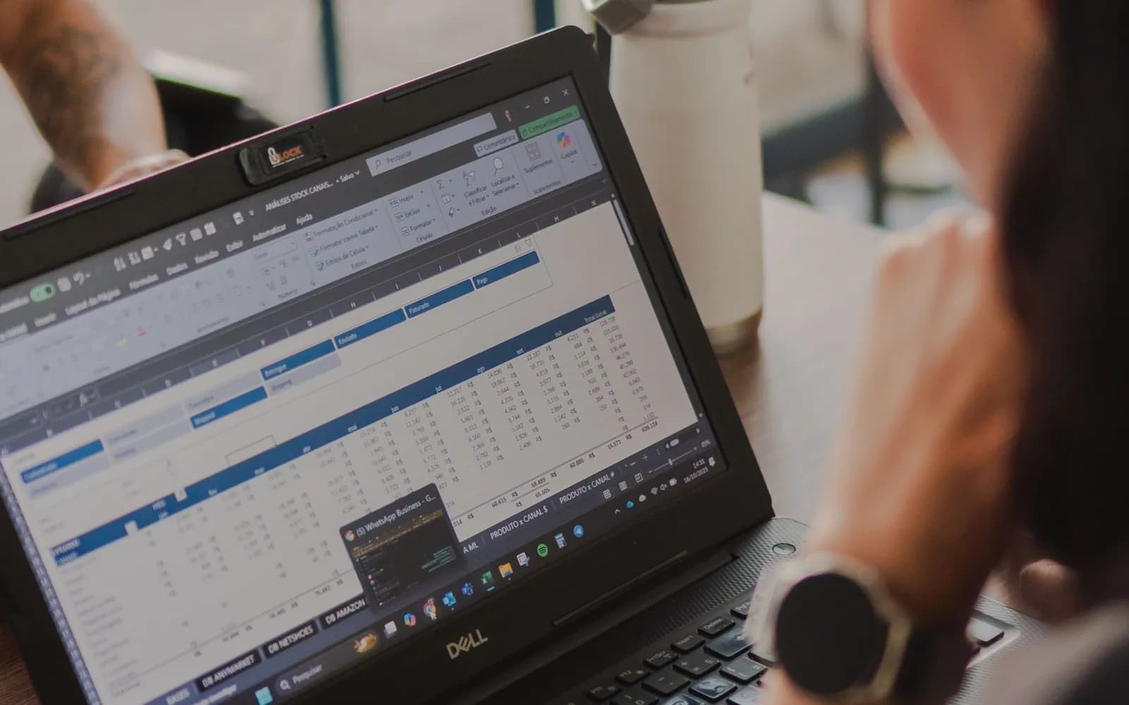 Close-up of a person reviewing a spreadsheet on a laptop in a cafe setting.