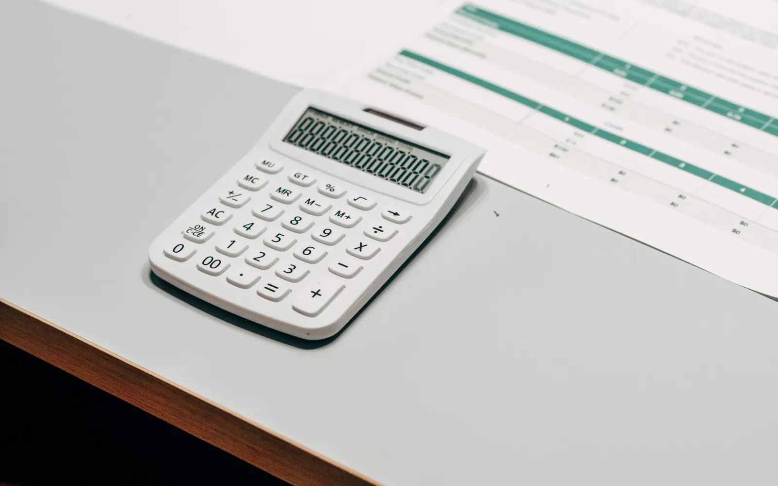 Close-up of a white calculator next to a financial spreadsheet on a desk.