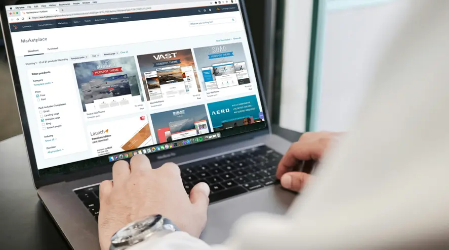 Hands on a laptop keyboard while the screen shows website themes in a marketplace